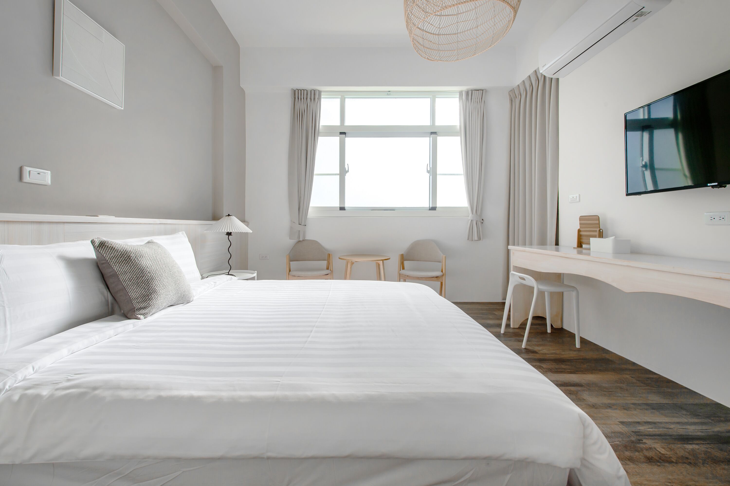 A modern hotel room with a large bed, a desk, two chairs, a TV, and a window with curtains.
