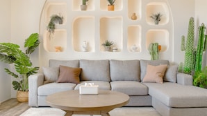 A modern living room with a grey sectional sofa, a round coffee table, and a wall-mounted plant shelf.