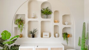 A white interior with a ceiling light, shelves with plants, a vase, and a framed picture.