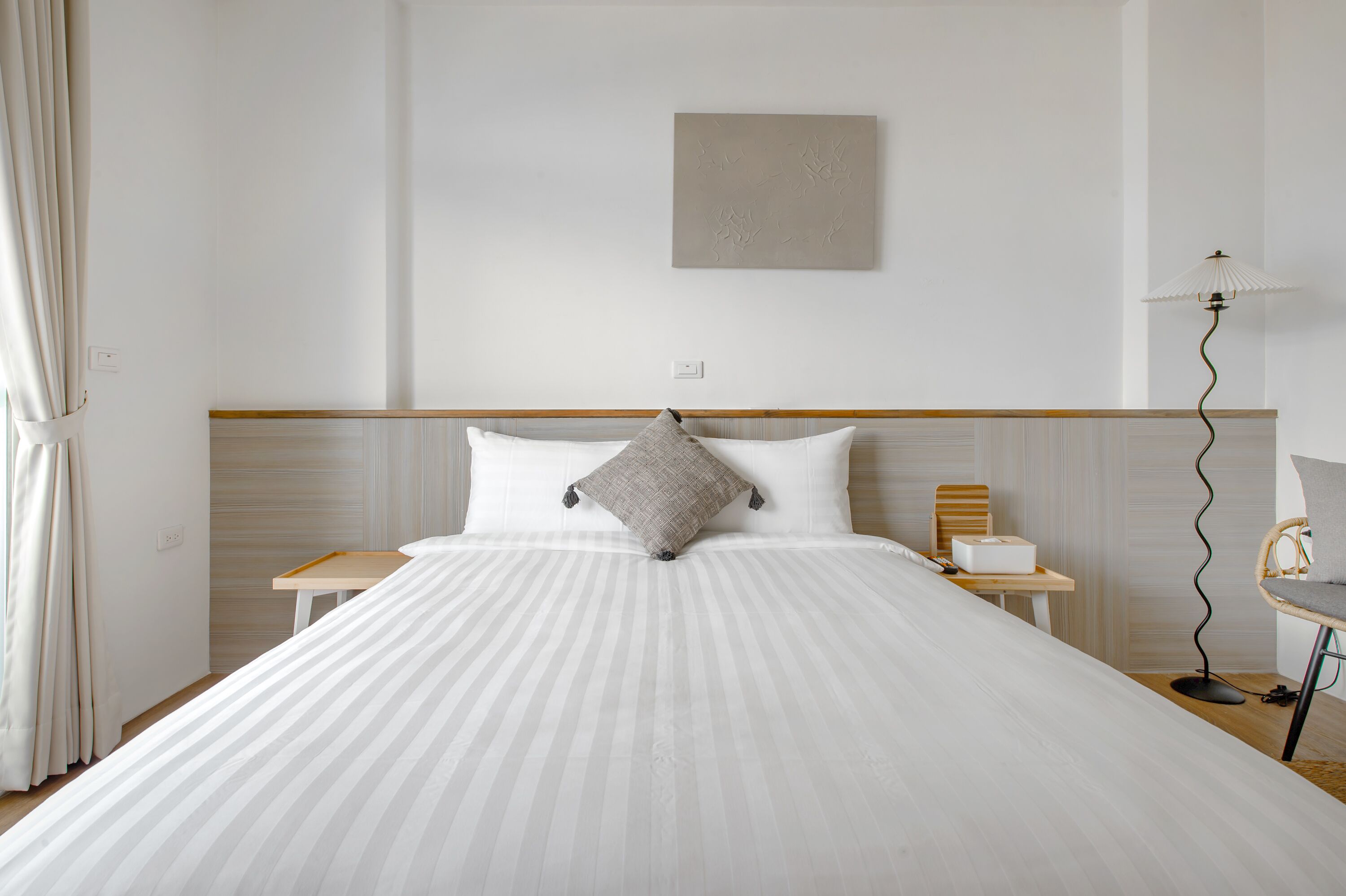 A neatly made bed with a striped bedspread, a single pillow, and a bedside table with a lamp.