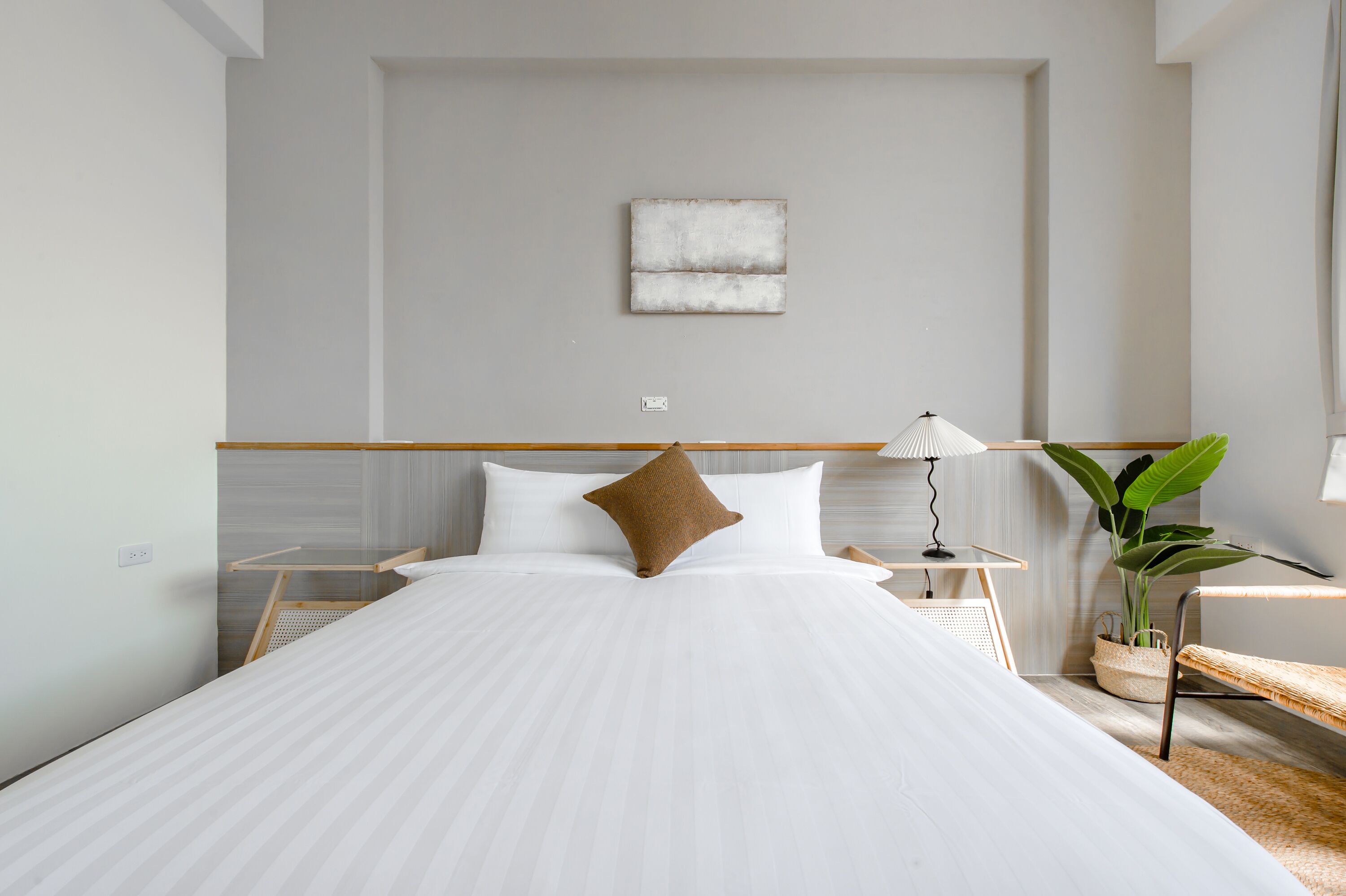 A modern hotel room with a large bed, a bedside table, a lamp, and a potted plant.