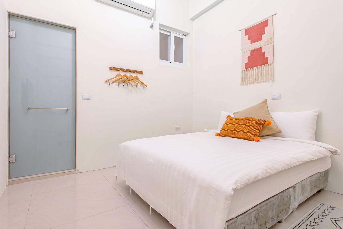 A bedroom with a bed, a door, a window, and a wall-mounted towel rack.