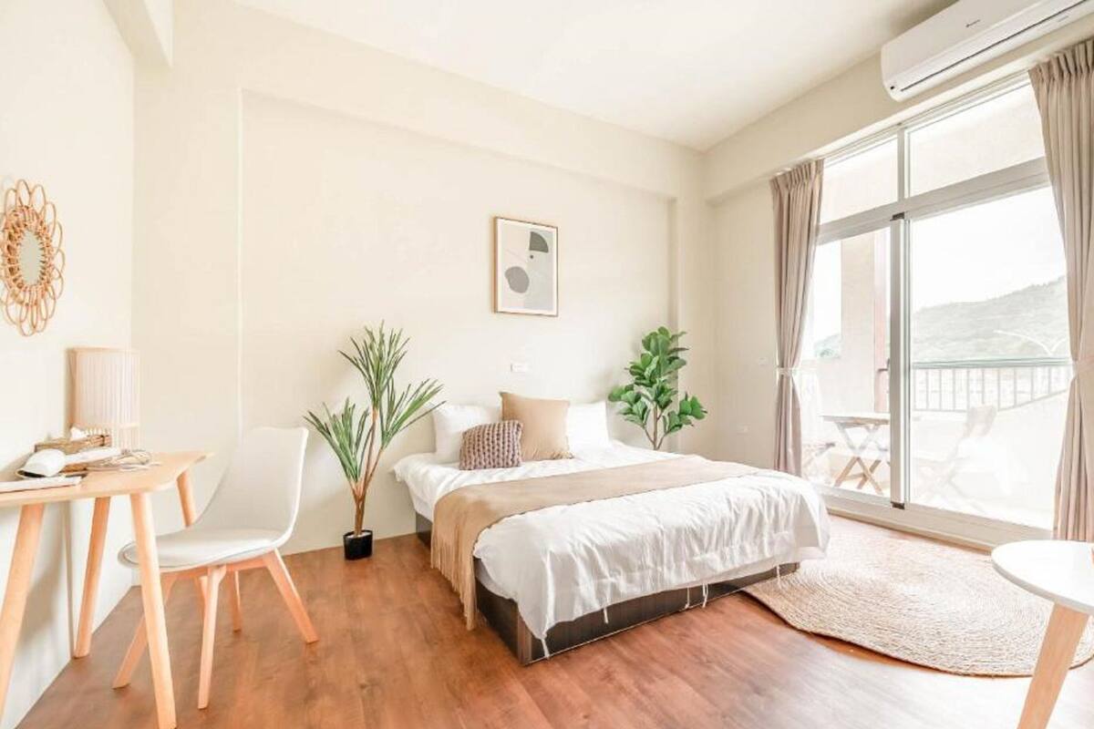 A modern bedroom with a bed, a desk, chairs, and a balcony with a view.