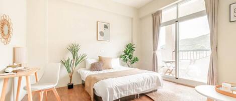 Un dormitorio moderno con cama, escritorio, sillas y balcón con vistas.