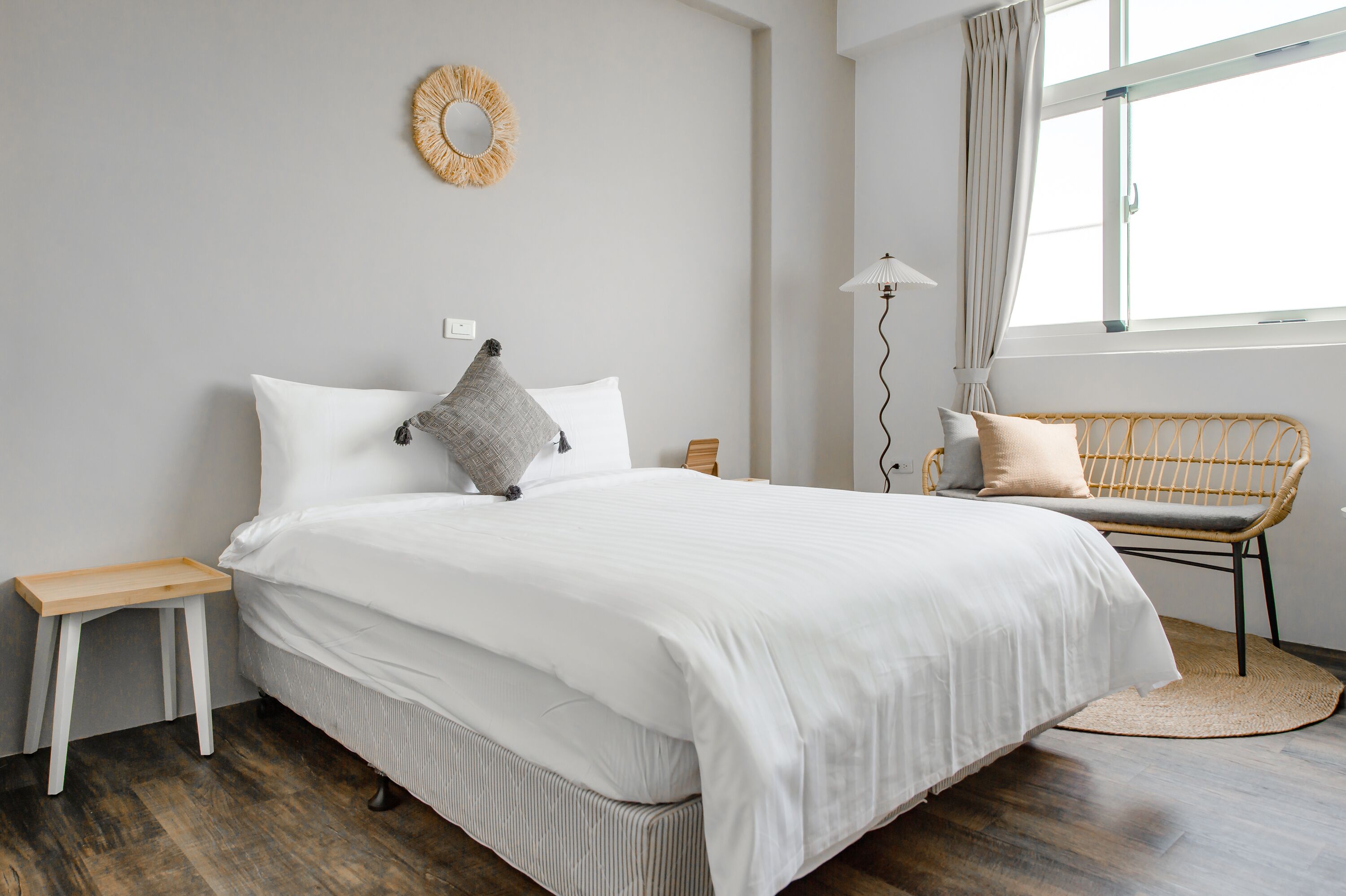 A neatly arranged bedroom with a large bed, a bedside table, a wicker chair, and a floor lamp.