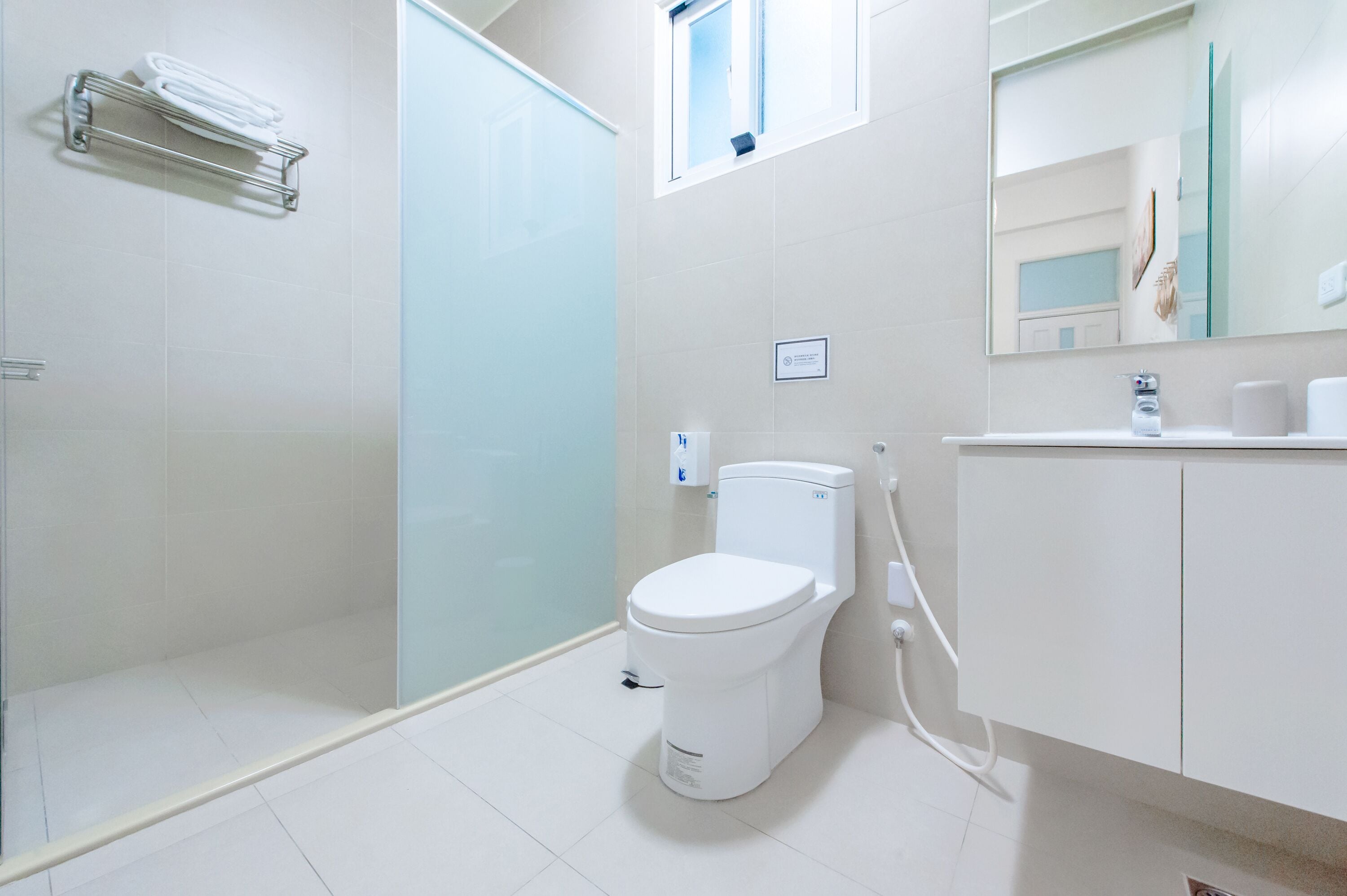 A modern bathroom with a toilet, a glass shower enclosure, and a white sink with a mirror above it.