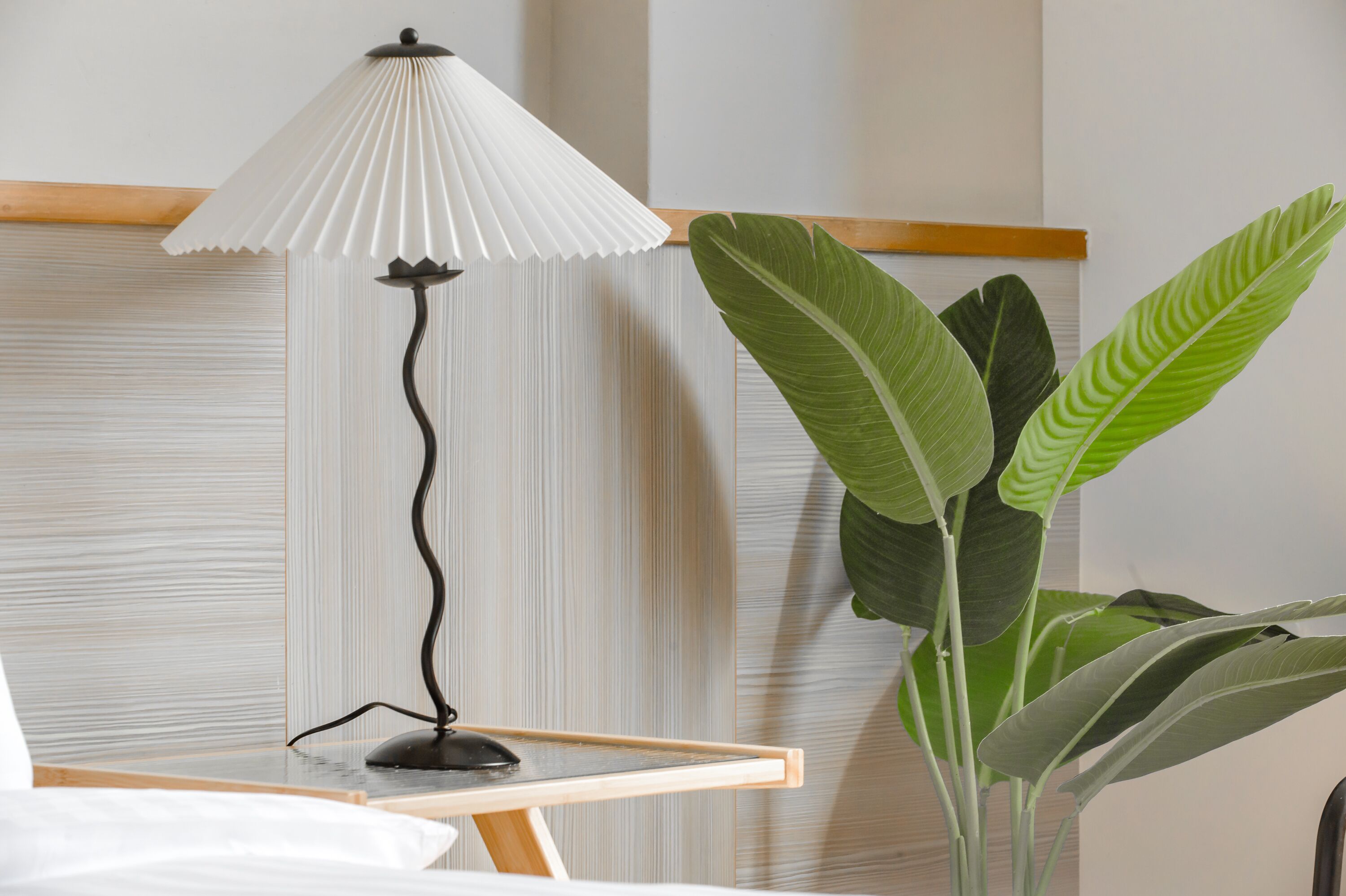 Una habitación con una cama, una mesita de noche con lámpara y una planta verde grande.