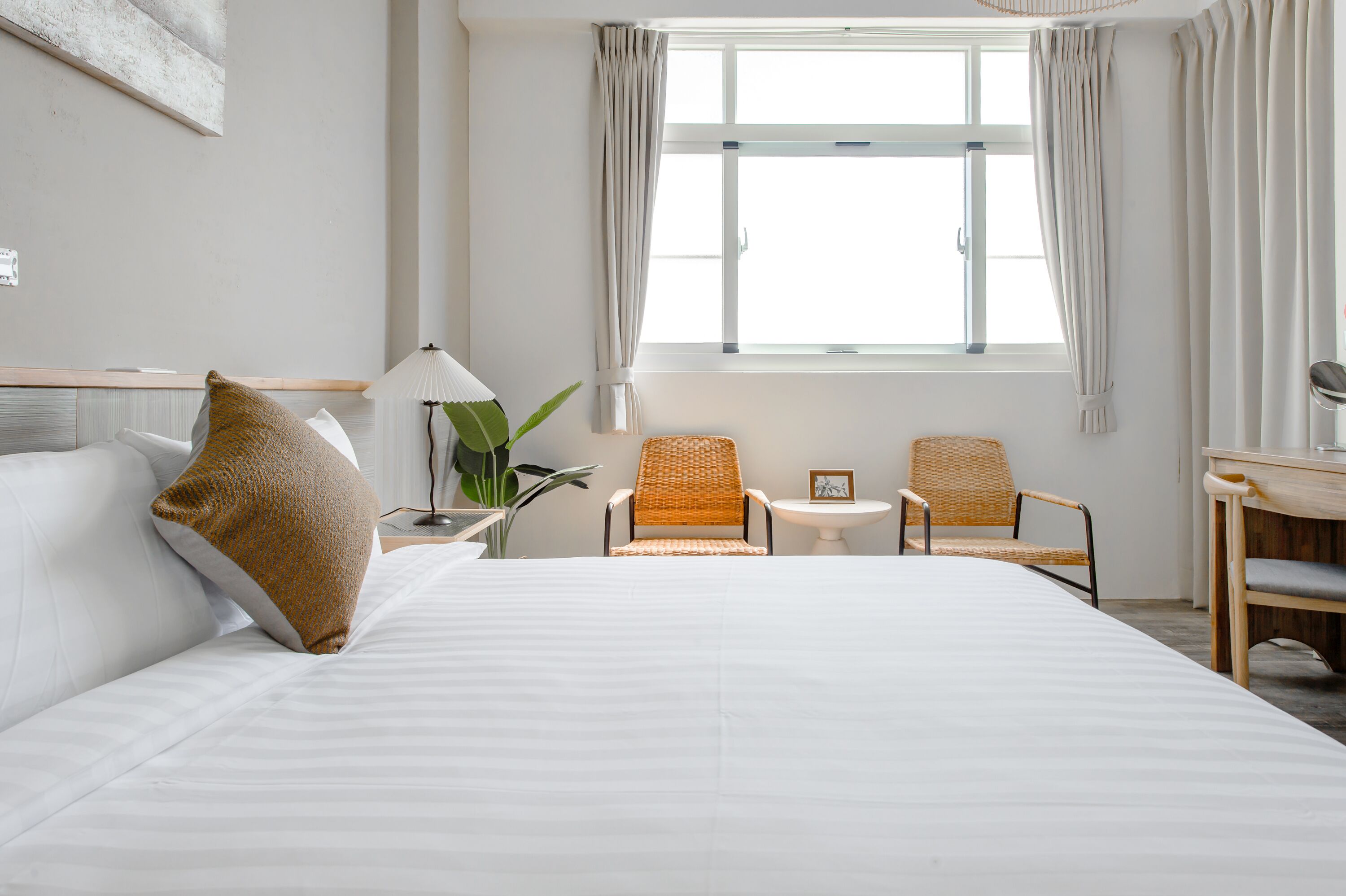 A hotel room with a large bed, two armchairs, a small table, and a window with curtains.