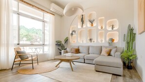 A modern living room with a sofa, a round coffee table, and a chair. There are plants and a cactus on the walls.