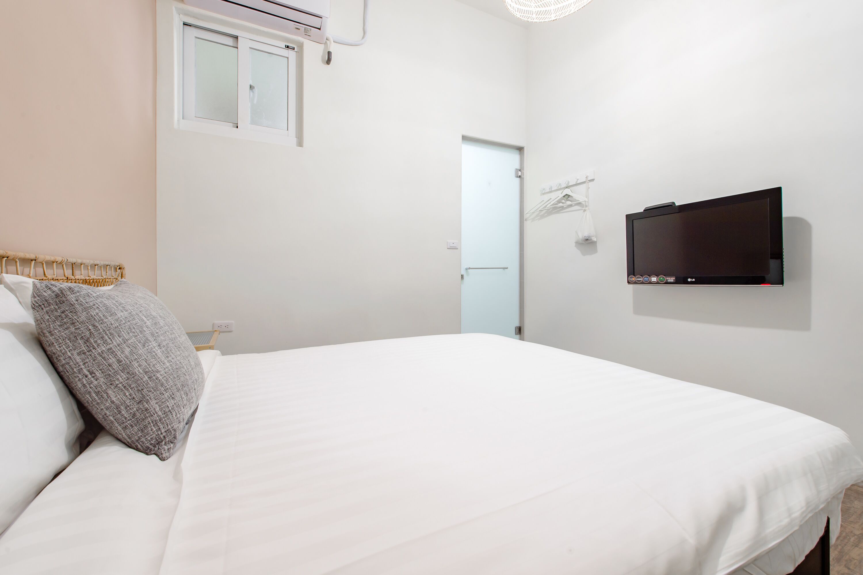 Un dormitorio con cama, televisión montada en la pared y ventana con unidad de aire acondicionado.
