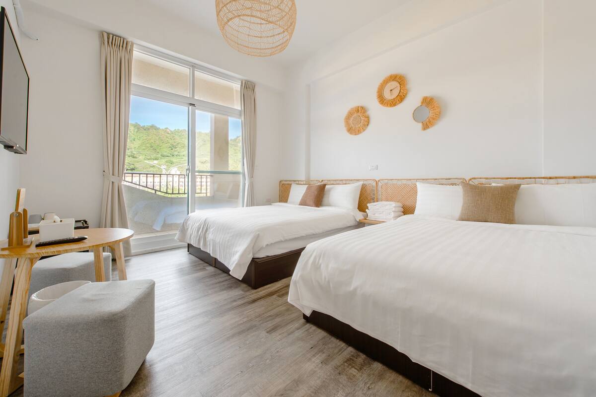 A hotel room with two beds, a balcony, a small table, and a chair.