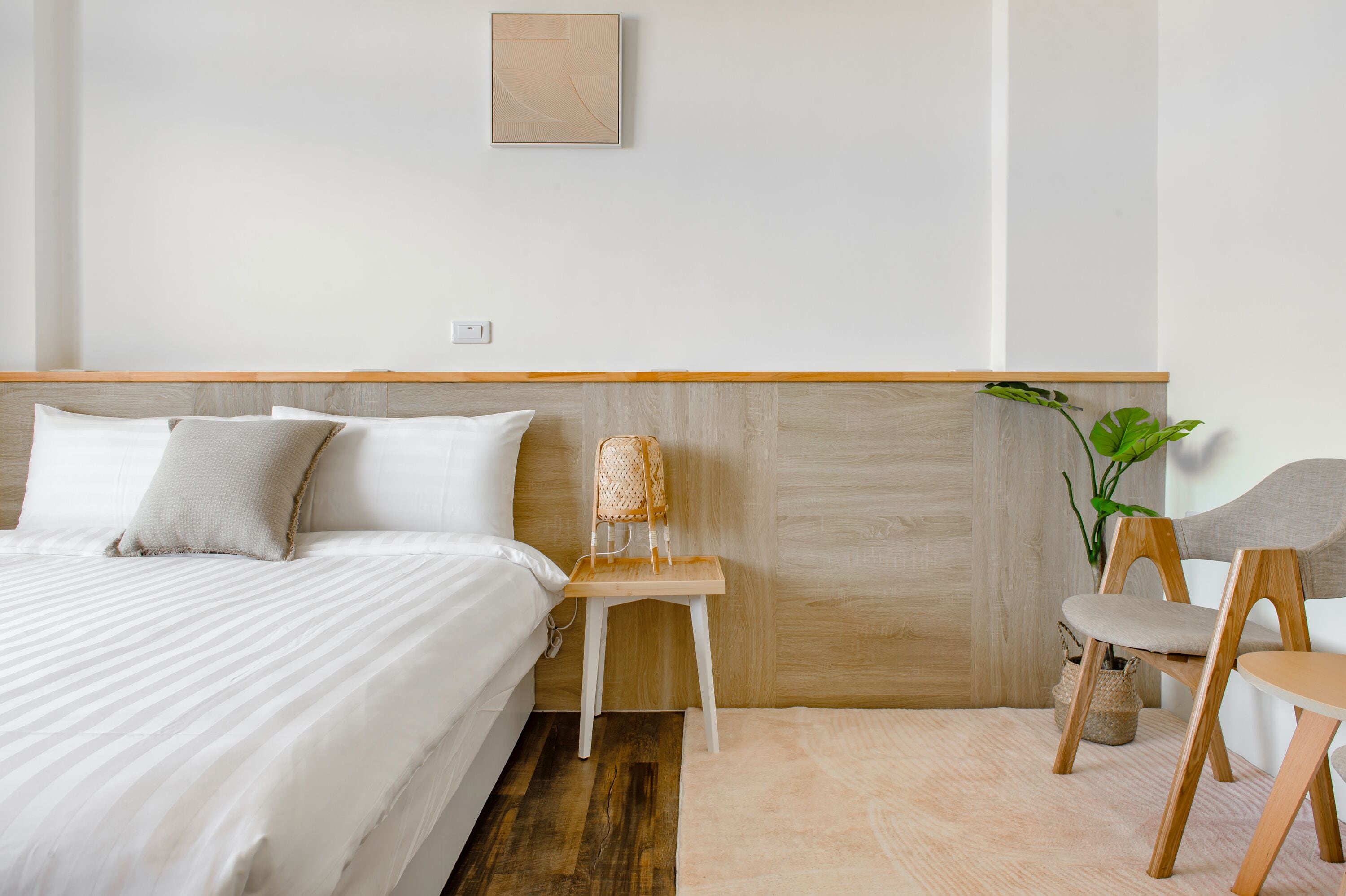 A bedroom with a bed, bedside table, chair, and a potted plant.