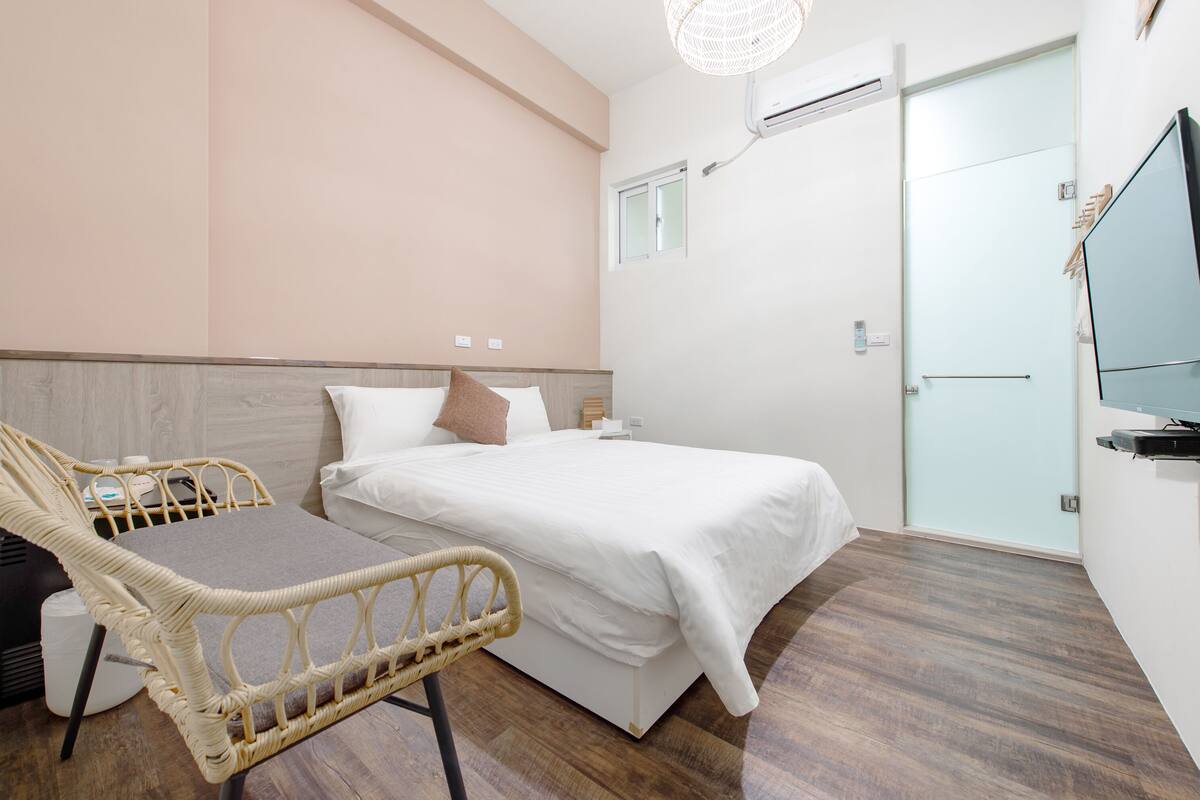 A bedroom with a bed, a chair, a television, and an air conditioning unit.
