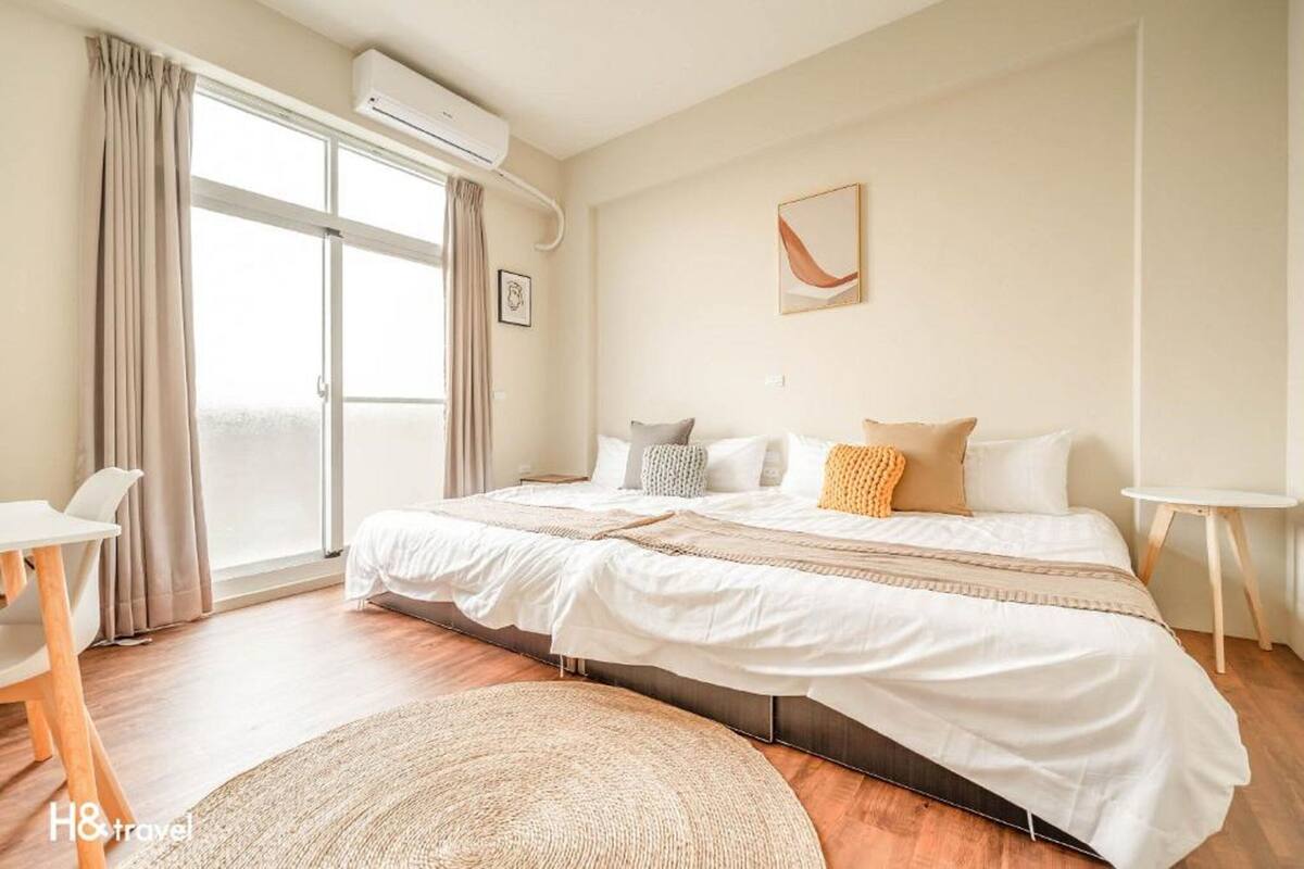 A bedroom with a large bed, a desk, and a window with curtains.