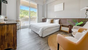 A modern hotel room with a large bed, a wooden desk, a comfortable armchair, and a view of the outdoors.
