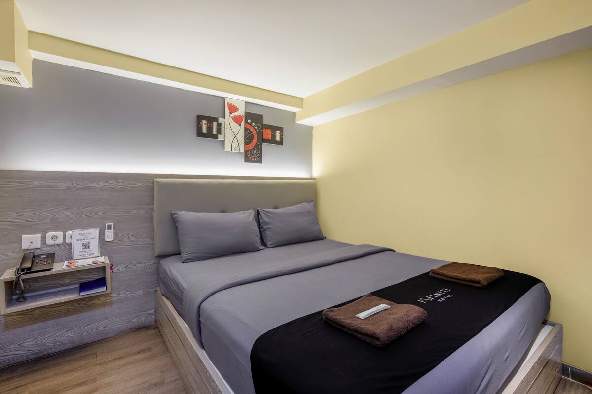 A modern hotel room with a bed, a bedside table with a phone, and a wall-mounted artwork.