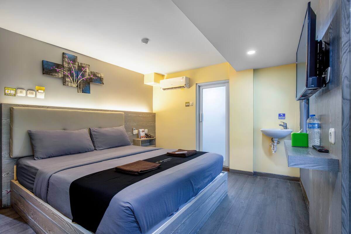 A modern hotel room with a large bed, bedside table, and a mounted TV.