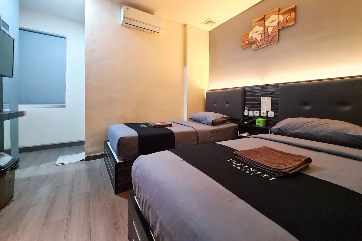 A hotel room with two beds, a flat-screen TV, an air conditioner, and a wooden art piece on the wall.