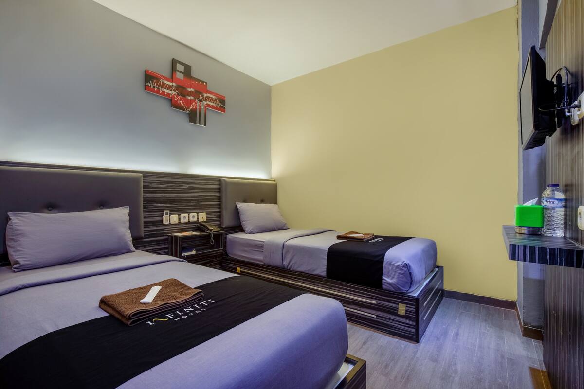 A hotel room with two beds, a flat-screen TV, a minibar, and a wall-mounted artwork.