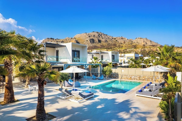 A resort with a swimming pool, lounge chairs, and palm trees.