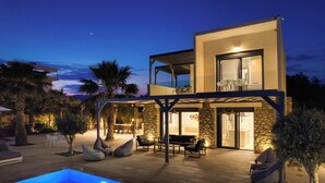 A modern two-story house with a pool, outdoor seating, and a well-lit patio area.