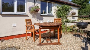 Ein Haus mit einer Terrasse, ausgestattet mit einem Holztisch und Stühlen, einem Grill und hängenden Blumenkörben.