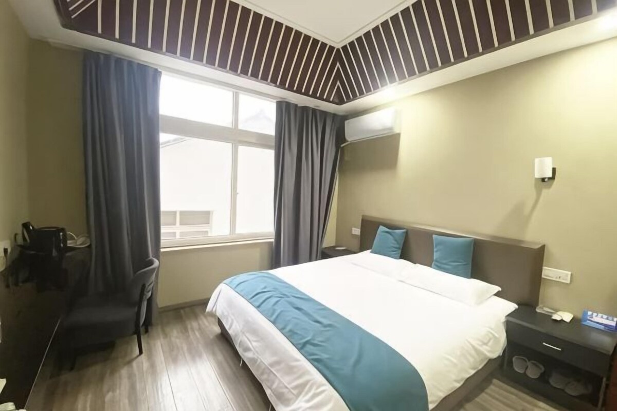 Una habitación de hotel con cama, mesita de noche, escritorio, silla y ventana con cortinas.