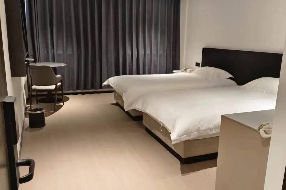 A hotel room with a bed, bedside tables, a chair, and a curtain.