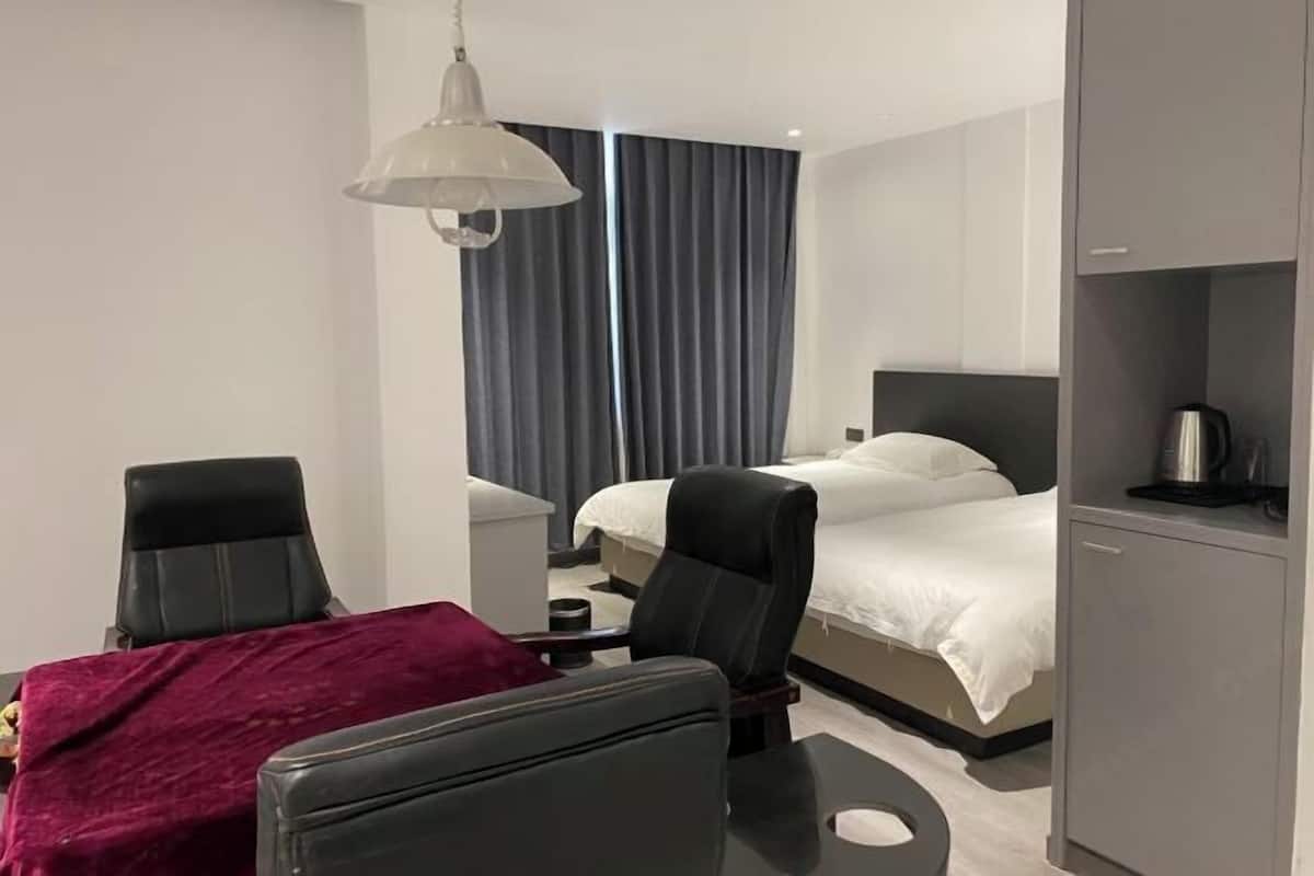 A modern hotel room with a bed, two chairs, a desk, and a minibar.