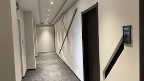 Un pasillo con alfombra gris, paredes blancas y una puerta negra con un letrero.