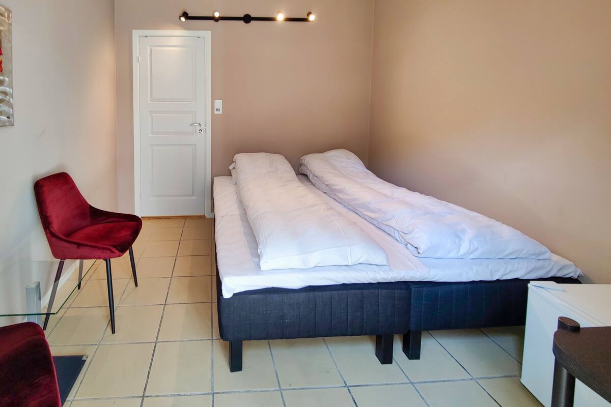 A small, neatly arranged room with a single bed, a chair, and a door.