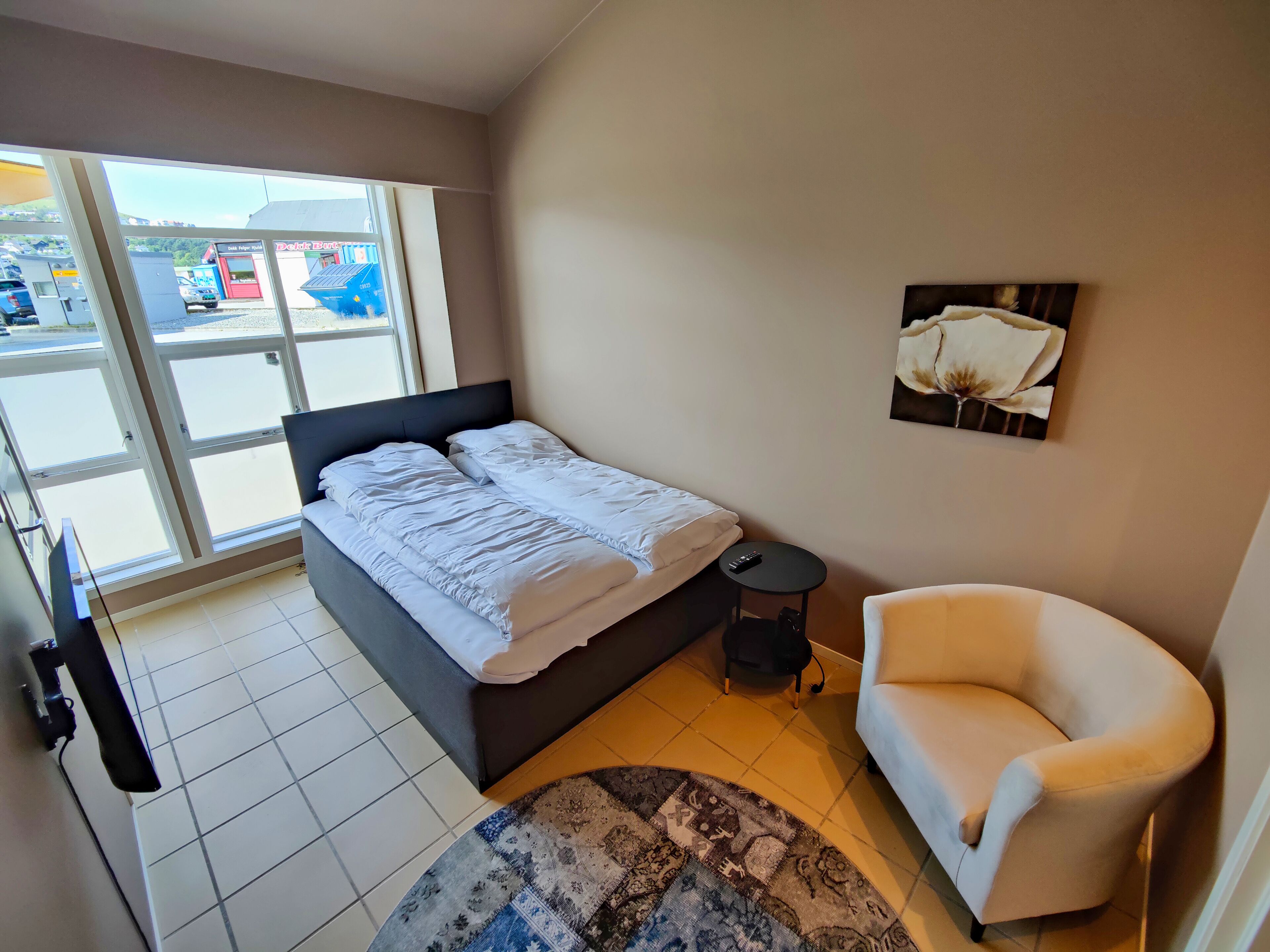 Een slaapkamer met een bed, een stoel, een klein tafeltje en een vloerkleed.