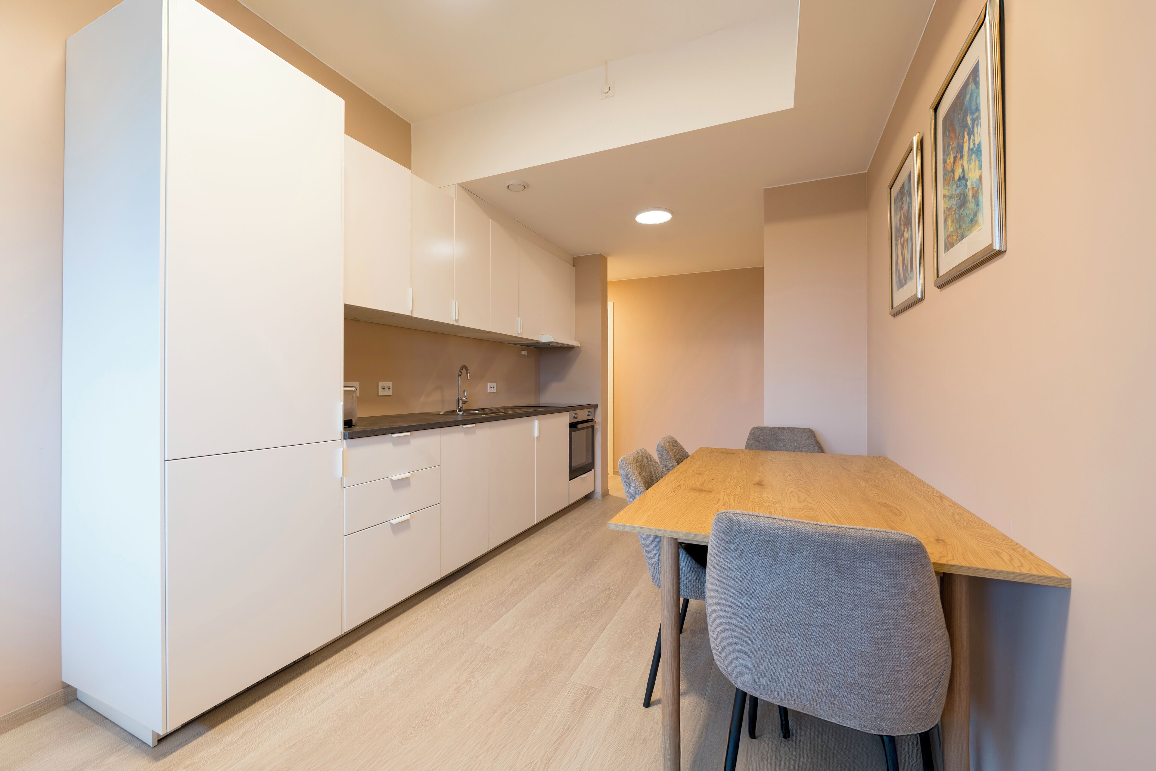 A modern kitchen with white cabinets, a wooden dining table, and grey chairs.