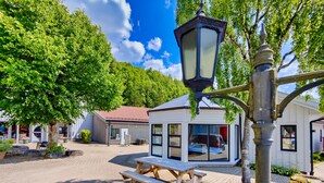 Een picknicktafel en banken in een zonnig buitengebied, met een gebouw op de achtergrond.