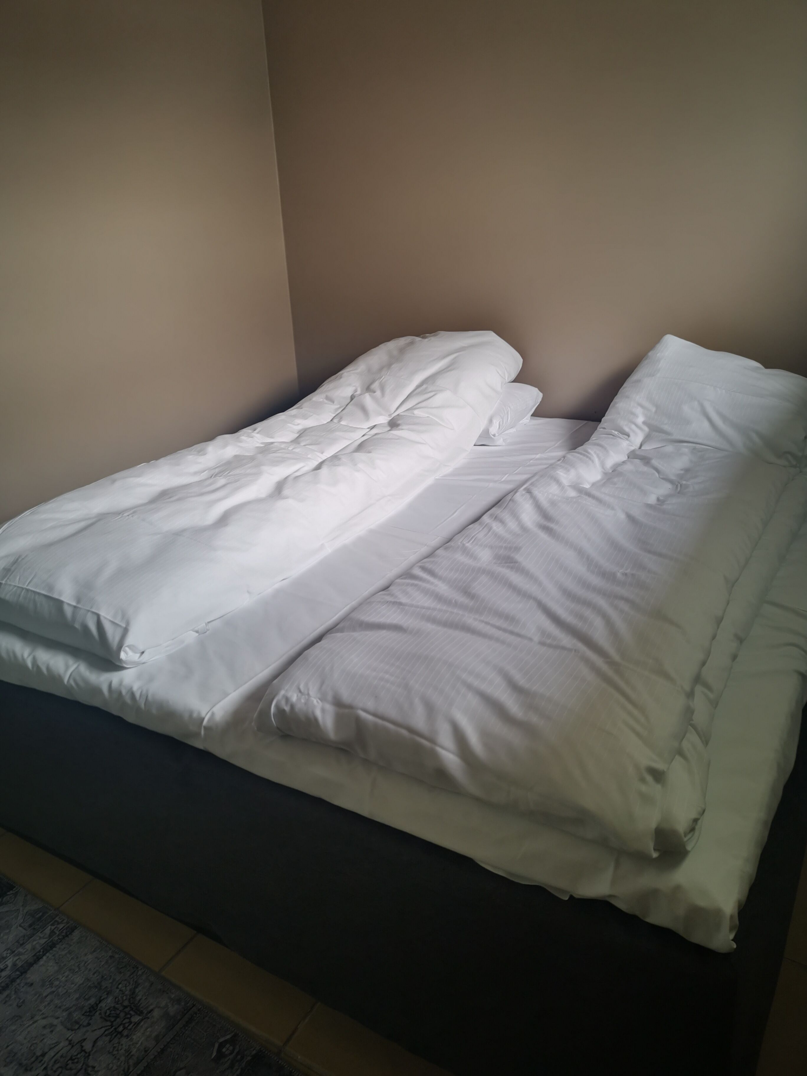 A bed with white bedding in a room with beige walls.
