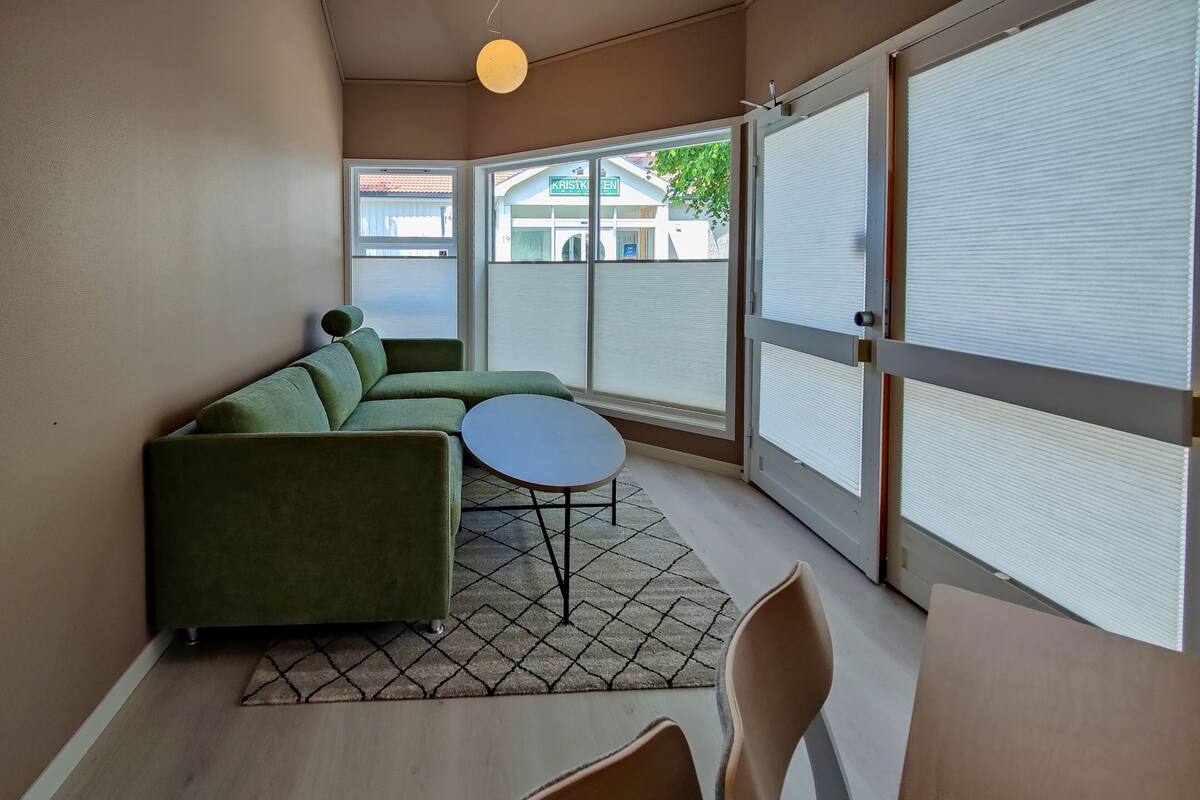 A modern living room with a green sectional sofa, a round coffee table, and a dining area with a table and chairs.