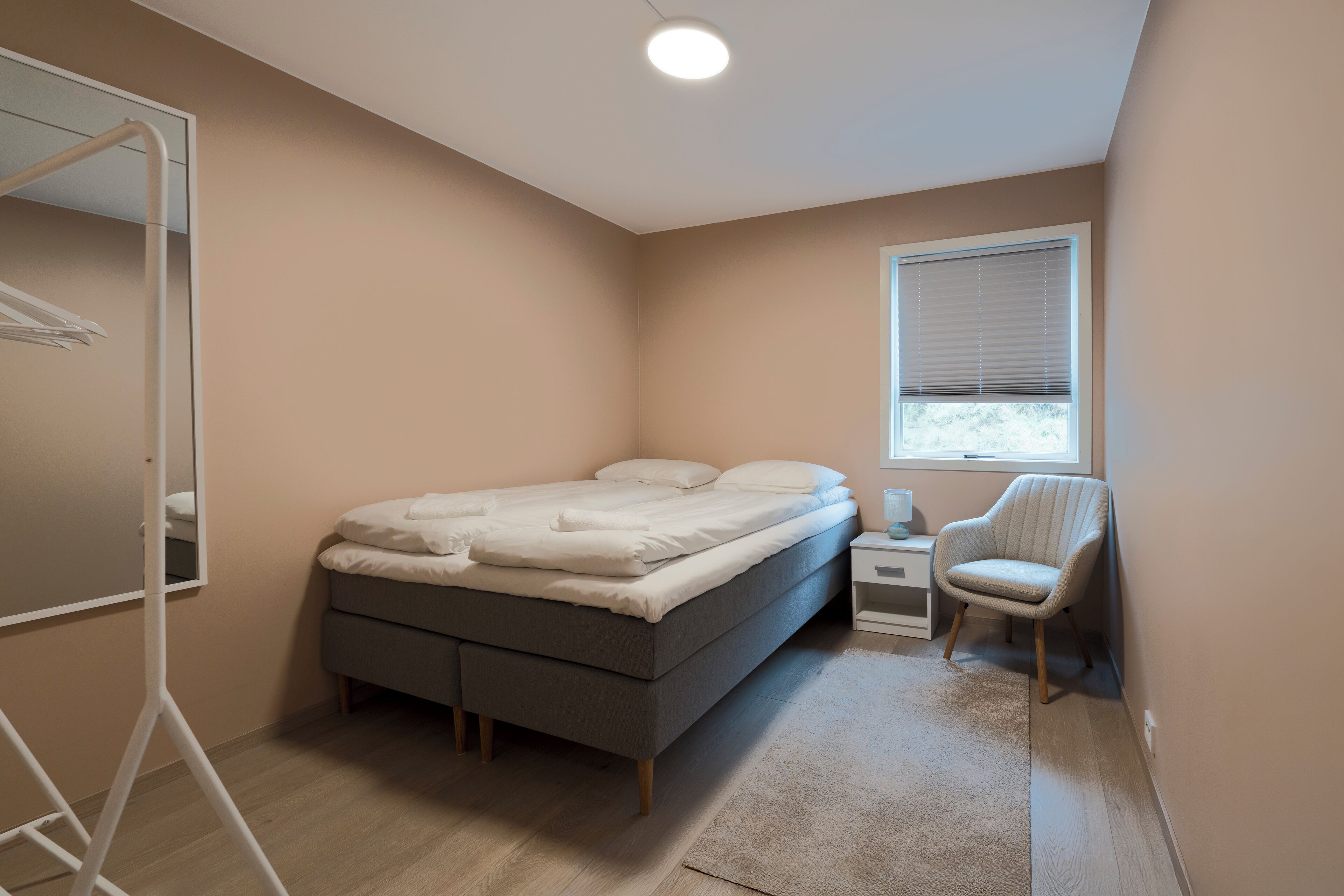 A bedroom with a bed, bedside table, chair, and a window with blinds.