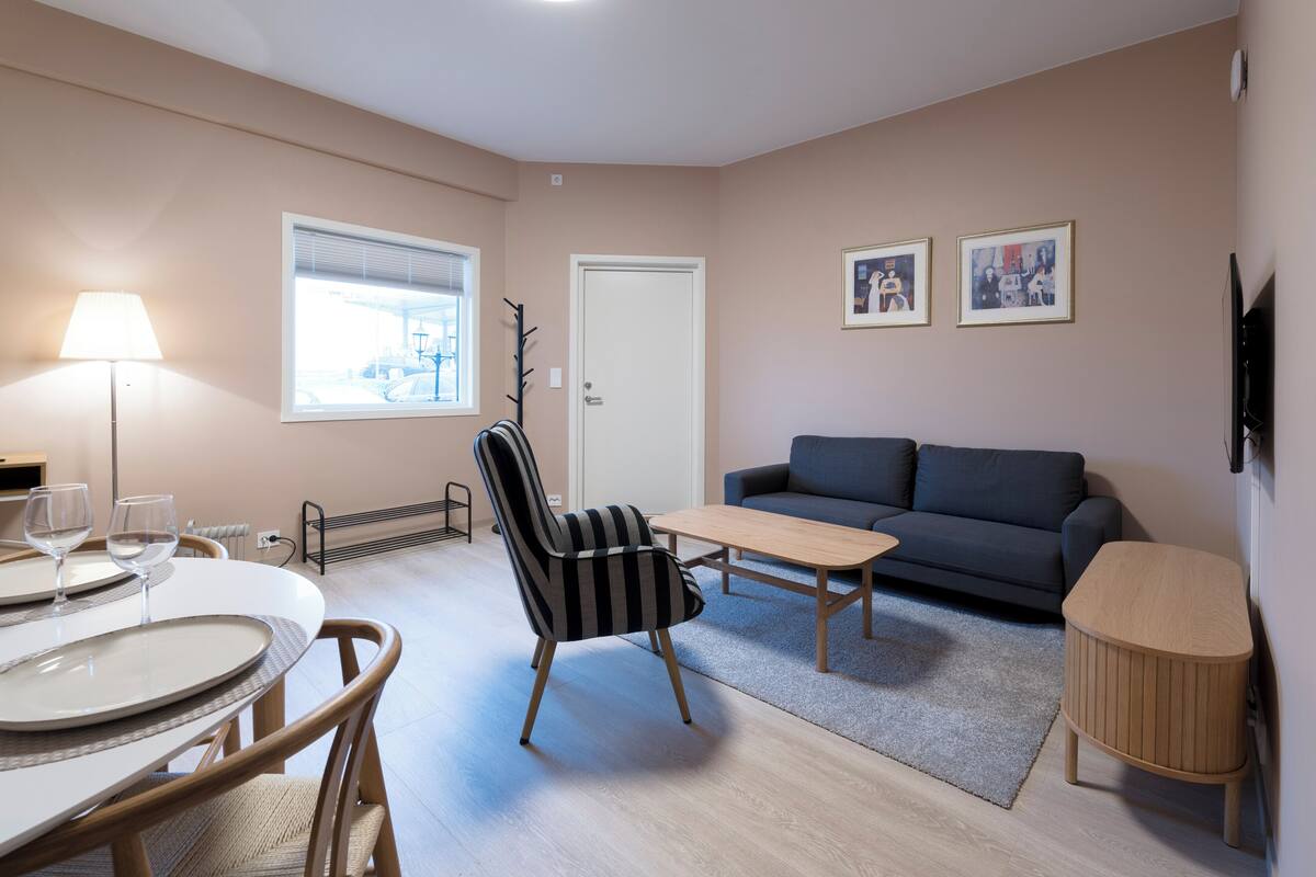 A modern living room with a dining table, striped armchair, sofa, and a small wooden side table.