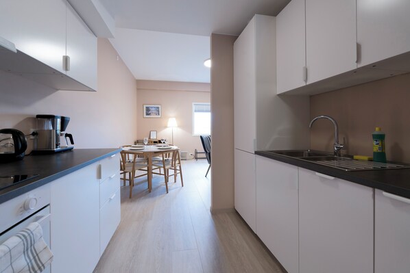 A modern kitchen with white cabinets, a black countertop, and a dining area with a table and chairs.