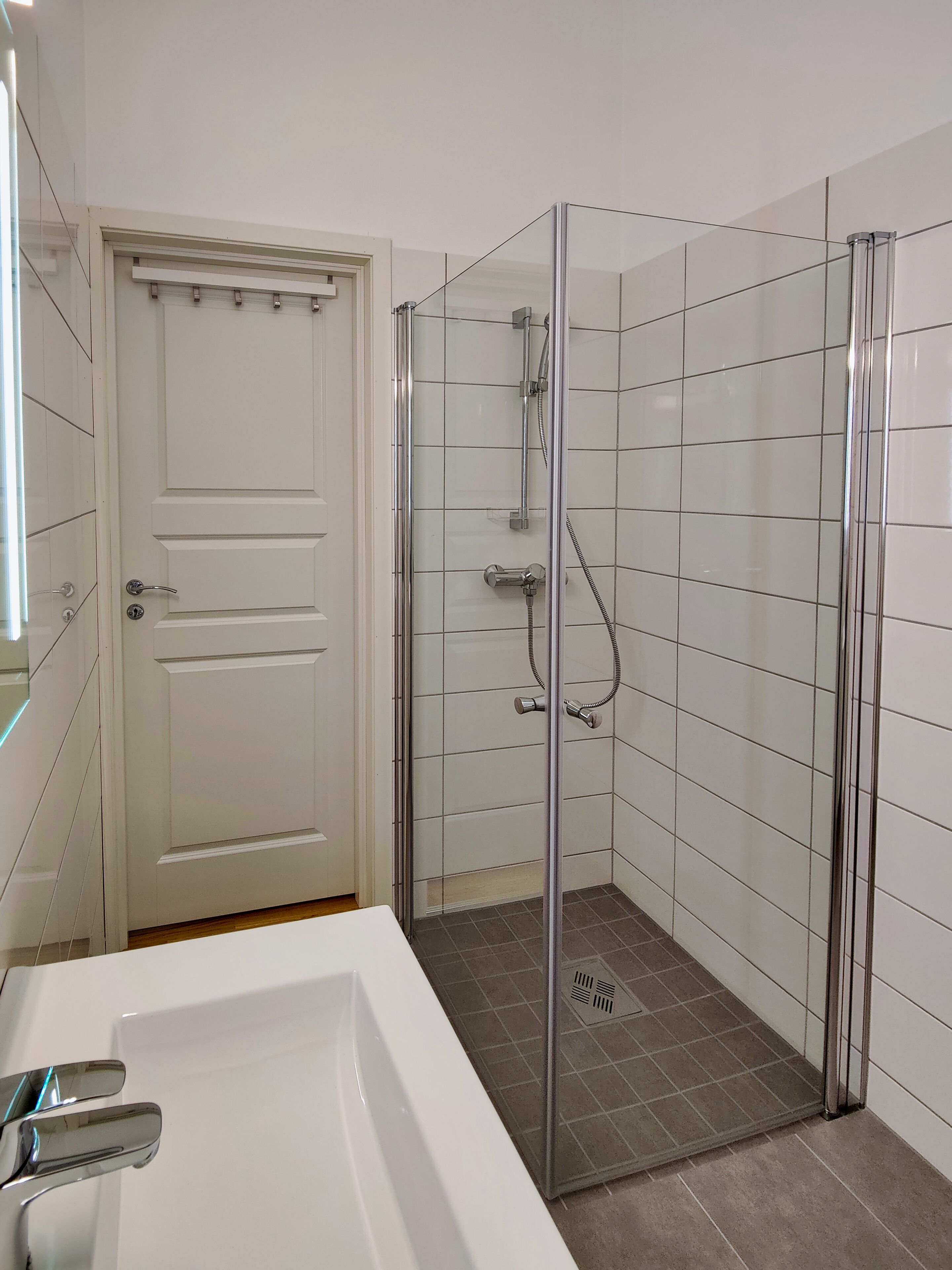 Un baño con ducha vidriada, lavamanos blanco y una puerta.