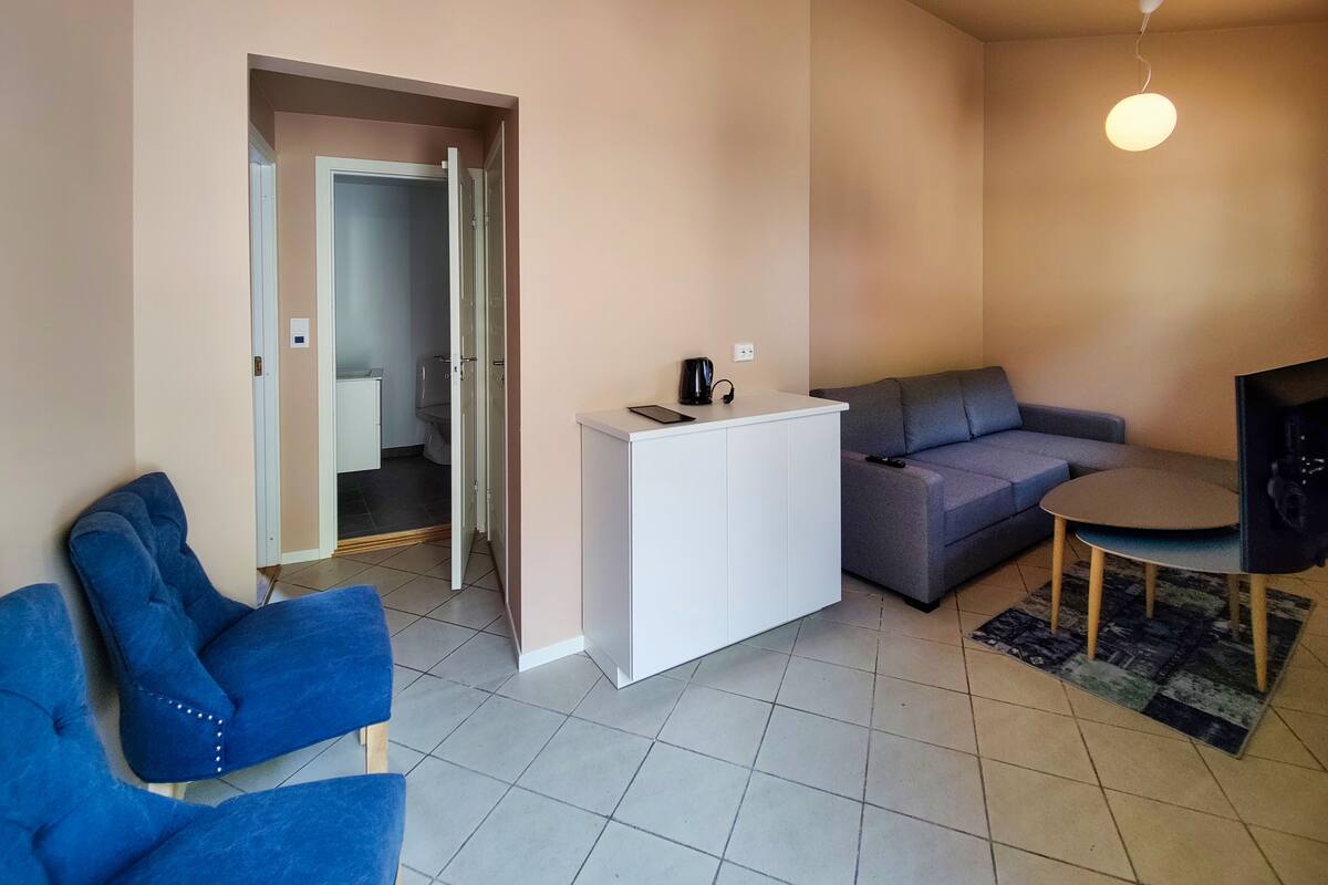 A modern living room with a sofa, a coffee table, and a TV. There is a door leading to a bathroom.