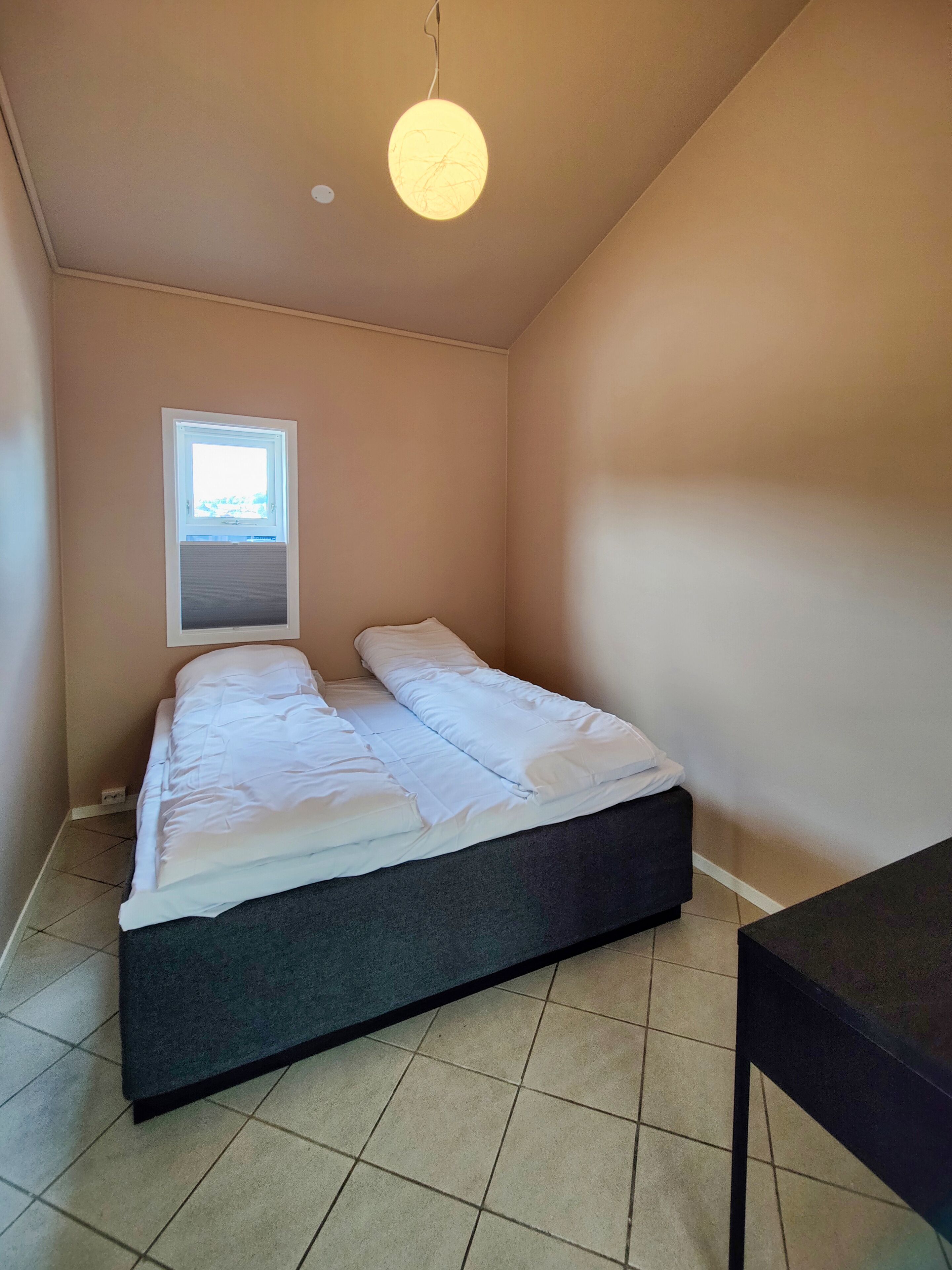 A small, neatly made bed in a room with a sloped ceiling and a window.