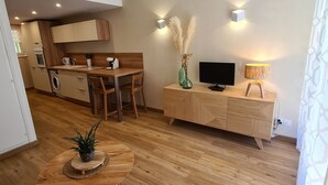 A modern living room with a wooden dining table, a TV, and a sofa. - Appartement au Calme Dans Residence Avec Piscine, Entouré de Foret (Bœrsch)