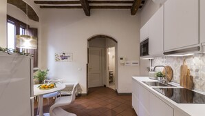 Cocina compacta con armarios blancos, salpicadero de azulejos y comedor con mesa y sillas blancas.