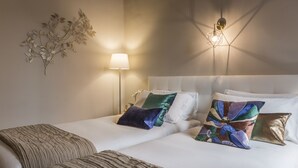 Una cama bien hecha con sábanas blancas y almohadas decorativas, una lámpara de noche y un aplique de pared.