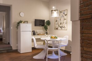 A compact kitchen with a refrigerator, a dining table with chairs, a TV mounted on the wall, and a geometric wall art piece. - Casa Dora by Mmega (Florence)