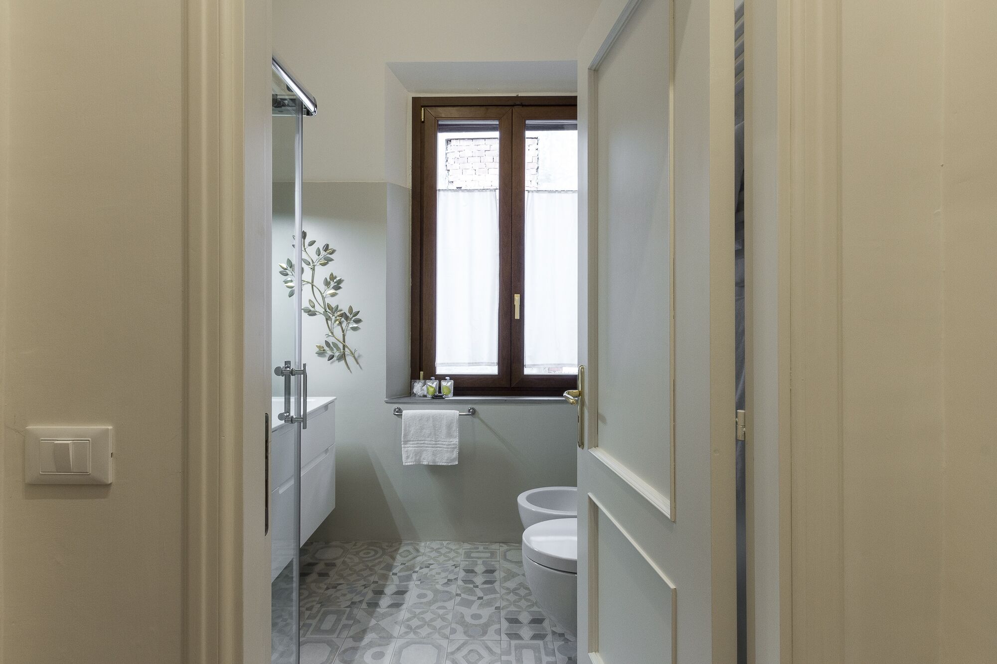 A narrow bathroom with a shower, toilet, and a window with curtains.