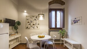 Cocina compacta con comedor, que incluye un refrigerador blanco, una mesa de comedor con sillas, una lámpara colgante y una ventana con cortinas.