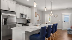 A modern kitchen with white cabinetry, stainless steel appliances, and a central island with blue chairs.