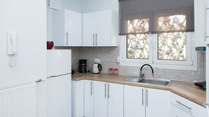 A modern kitchen with white cabinets, a wooden countertop, a coffee maker, and a window with a view of trees. - Chic apartment in Athens (Athens)